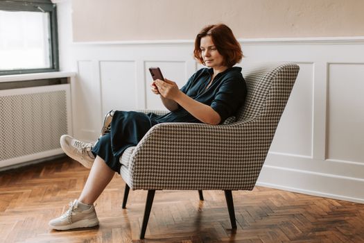 Woman sitting on chair indoors using smartphone, showcasing prosthetic leg. Calm and modern setting.