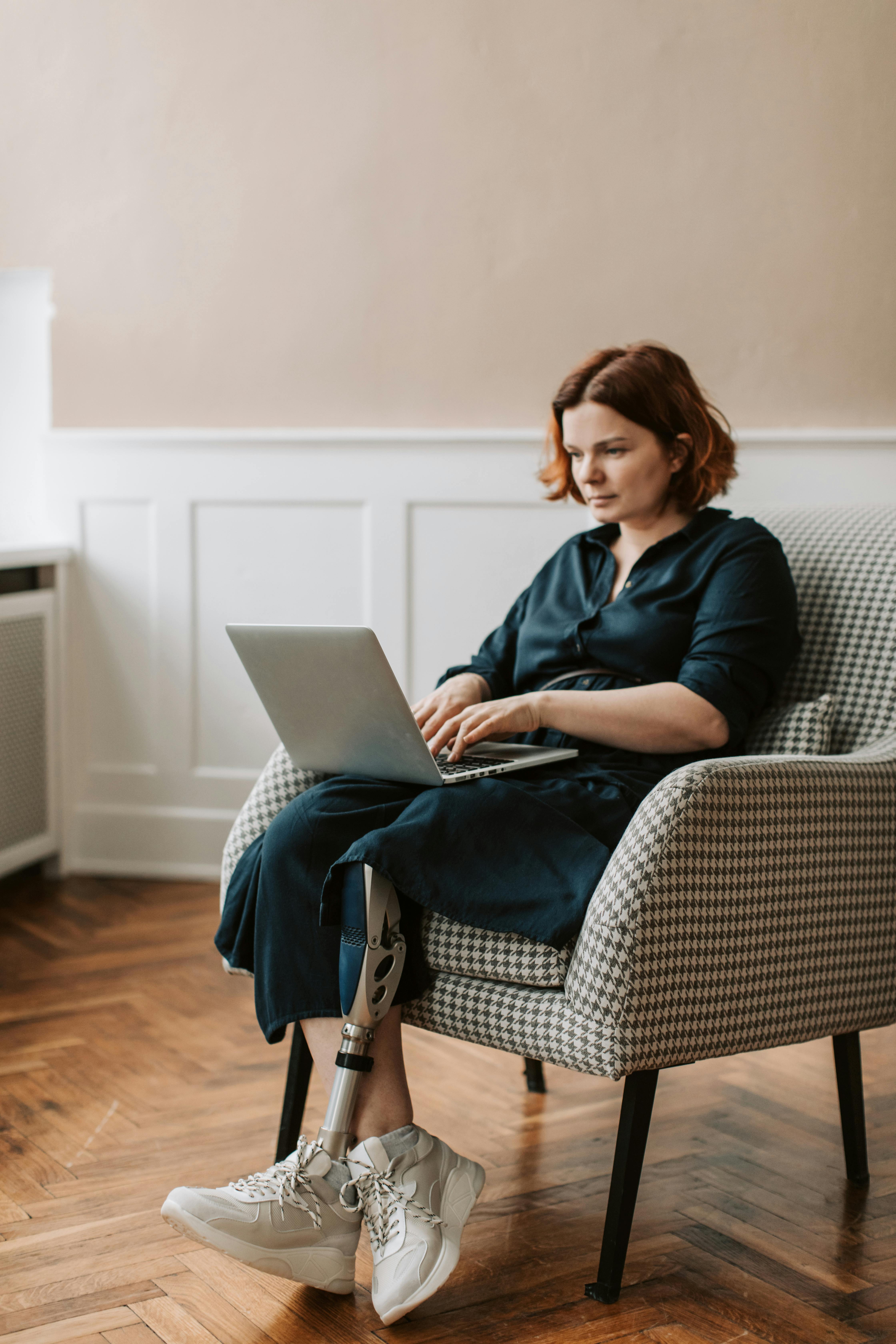 A Woman Sitting on the Plain Cover Chair Using a Laptop