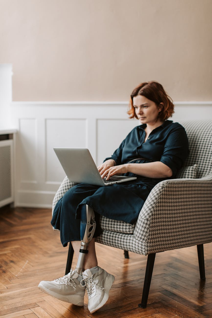 A Woman Sitting on the Plain Cover Chair Using a Laptop