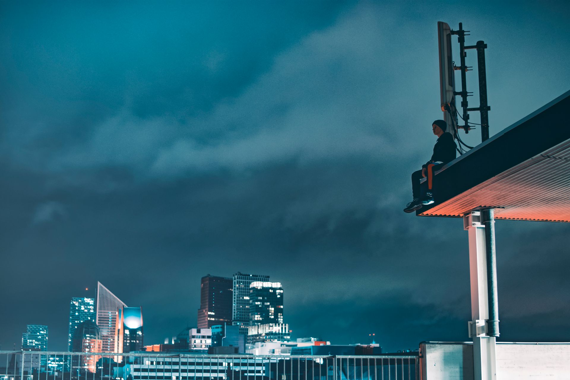A person sitting on a rooftop overlooking a city's illuminated skyline at night.
