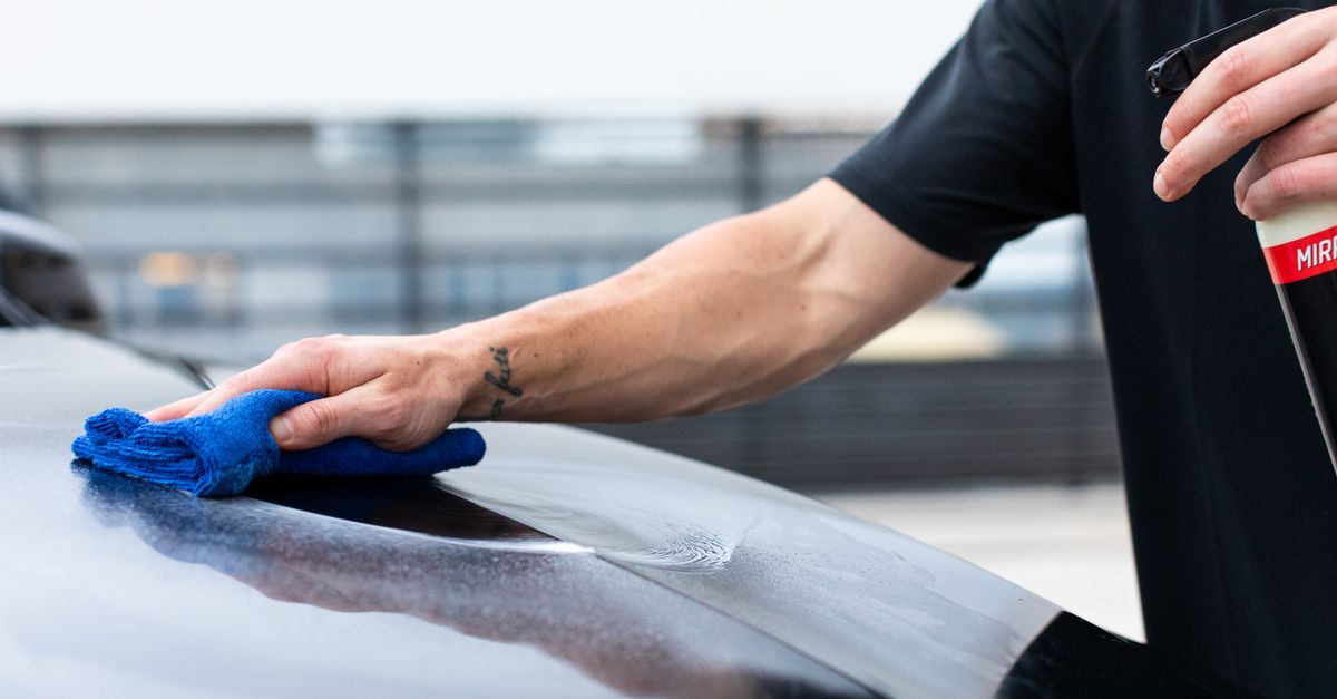 Close-up of hand cleaning car with cloth and spray bottle for maintenance.