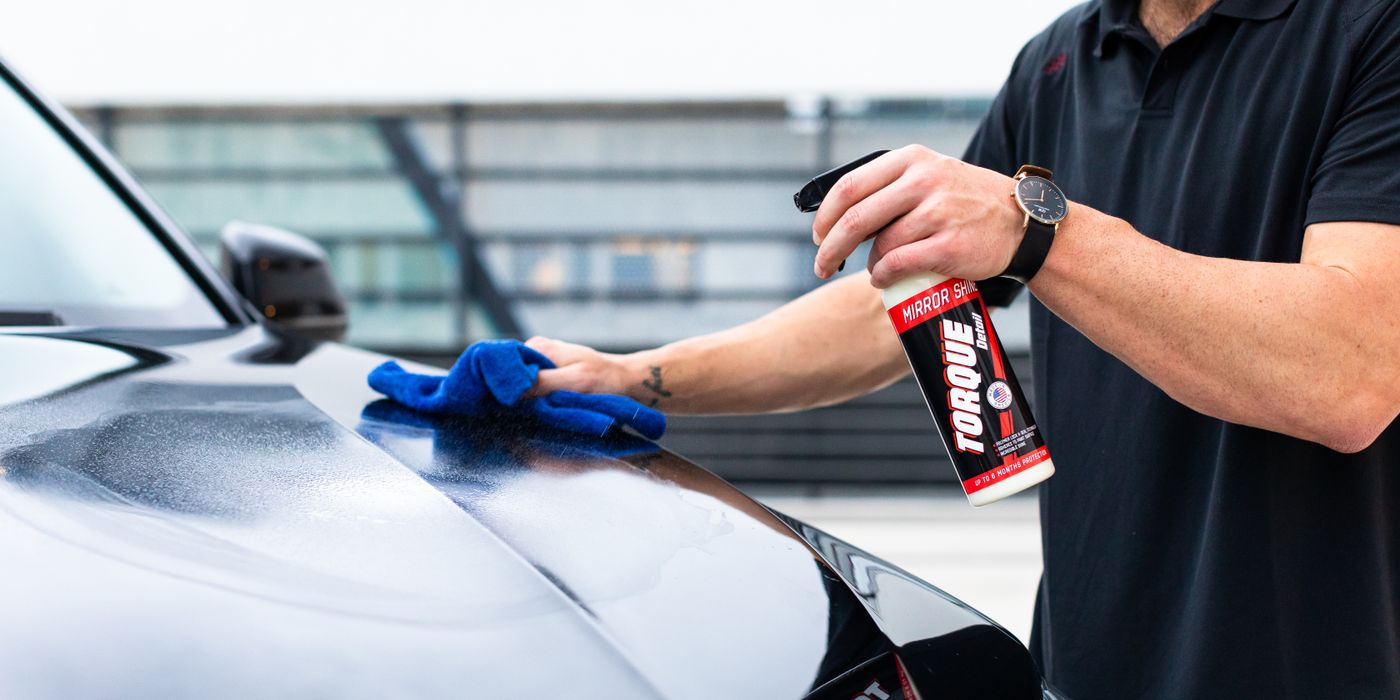A man spraying a hood and wiping it with a blue microfiber towel