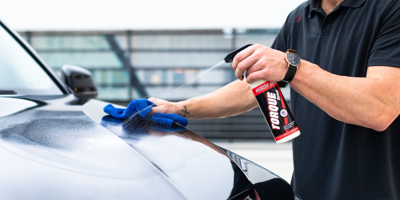 A man spraying a paint protection product onto a car and wiping it with a microfiber towel