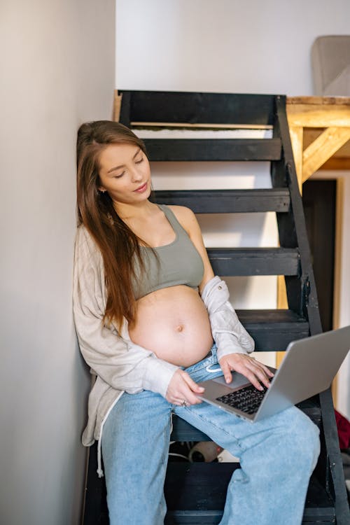 Pregnant Woman using Laptop while sitting on a Staircase