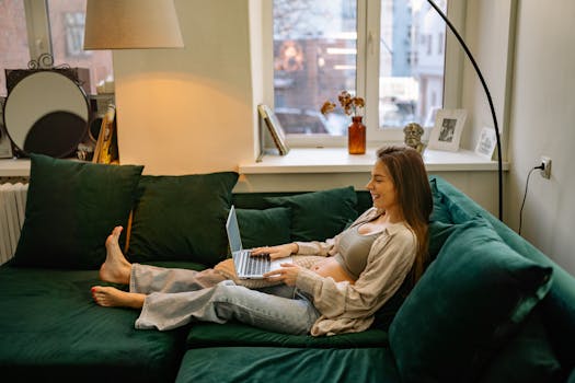 Expectant mother relaxing on sofa with laptop, enjoying remote work from home.