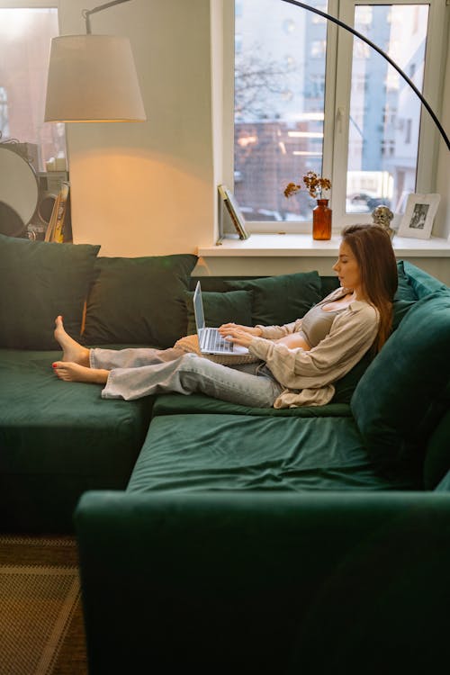 Free A Woman Sitting on a Green Sofa Using Her Laptop Stock Photo
