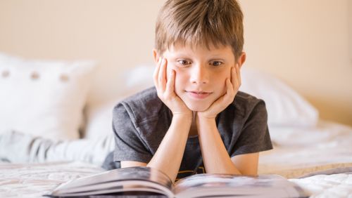 Free Young boy lying on bed, absorbed in a book, illustrating curiosity and learning. Stock Photo