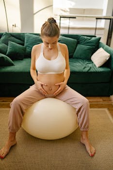 Expectant mother doing yoga on a gym ball in a cozy living room setting for healthy living.