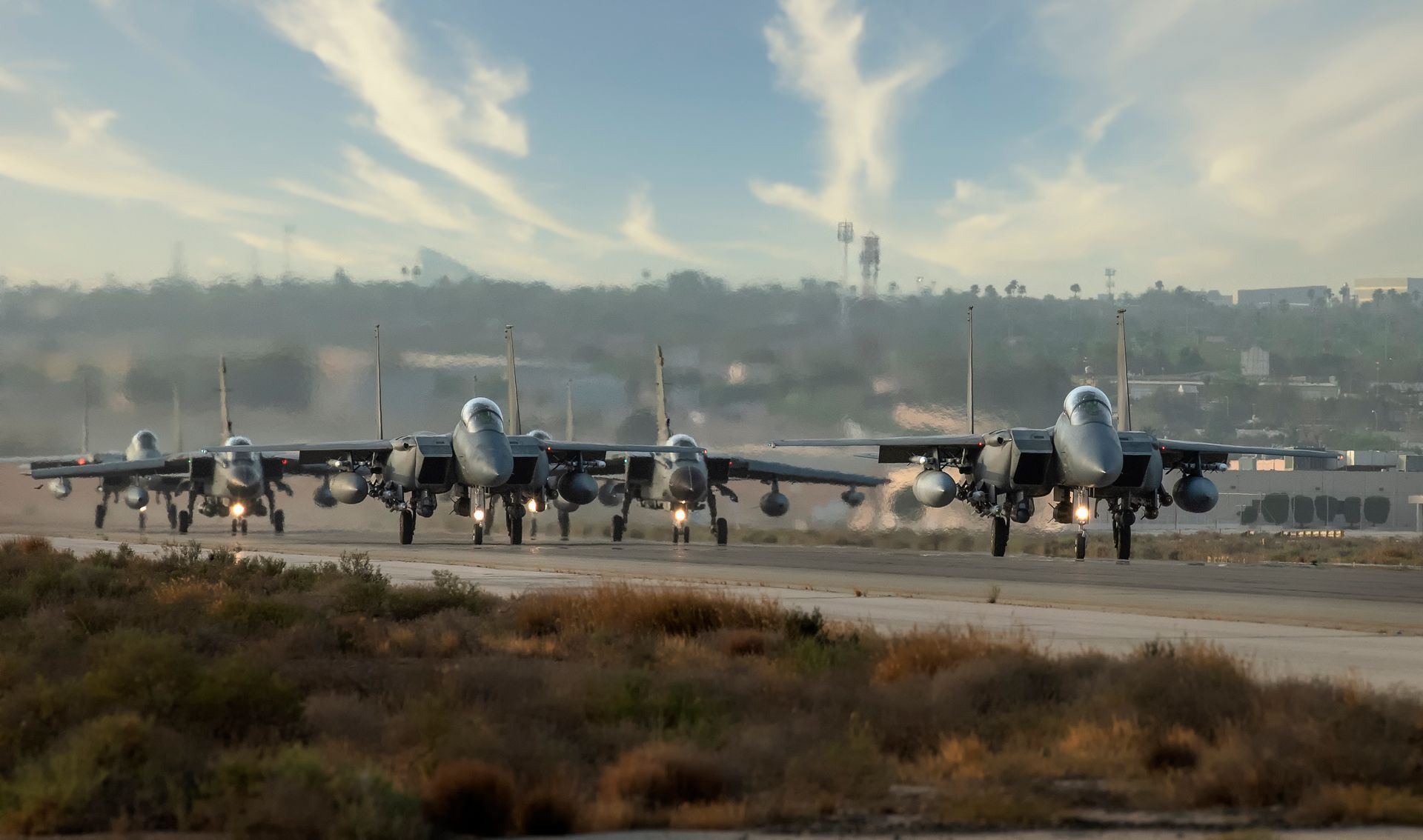 A fleet of military fighter jets prepares for takeoff on a runway under a clear sky.