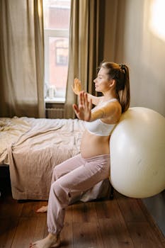 Expectant mother practicing yoga exercises indoors using an exercise ball.