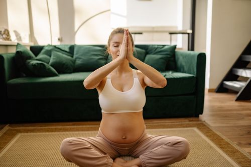 Free A pregnant woman in a peaceful yoga pose indoors, promoting positive wellness. Stock Photo