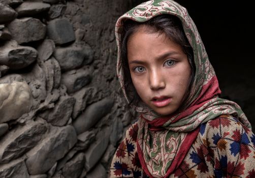 Close-up portrait of a young girl wearing a patterned headscarf, looking intently at the camera.