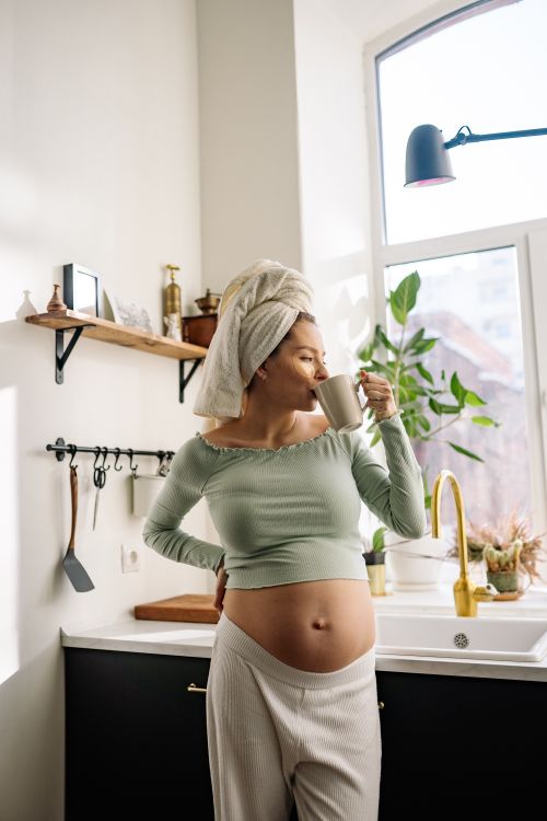 Free Pregnant woman in kitchen enjoying a hot drink, embracing relaxation and comfort. Stock Photo