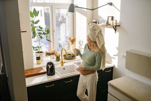Pregnant woman with head towel enjoying morning tea by the kitchen window.