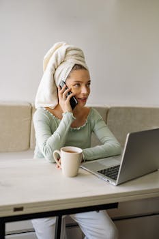 Caucasian woman combining remote work with self-care, using a laptop and phone.