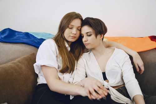 Free Two women embracing on a couch with a rainbow flag symbolizing LGBT pride. Stock Photo