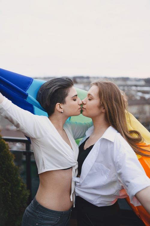 Free Intimate moment between a loving LGBTQ+ couple embracing under a pride flag. Stock Photo