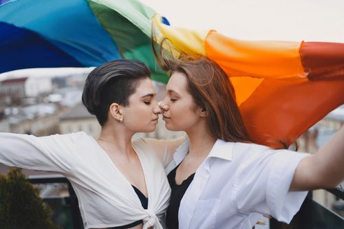 Free Two women embrace under a rainbow flag, symbolizing love and pride. Stock Photo
