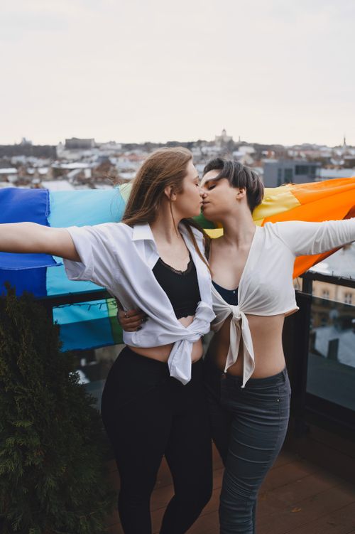 Free Two women embrace under a rainbow flag, symbolizing love and LGBTQ+ pride. Stock Photo