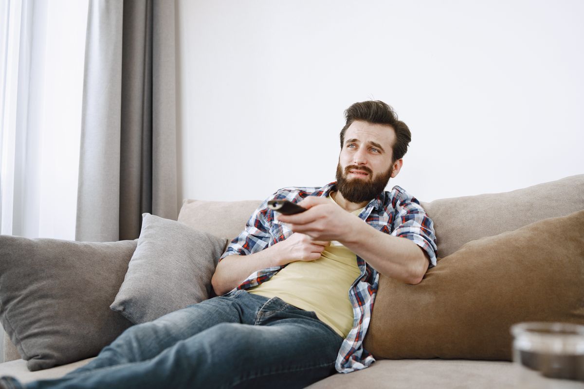 Mann bedient mit einer Fernbedienung einen Fernseher im Wohnzimmer