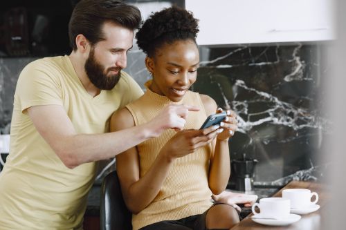 Free A smiling couple enjoying a moment together while looking at a smartphone indoors, signifying togetherness. Stock Photo