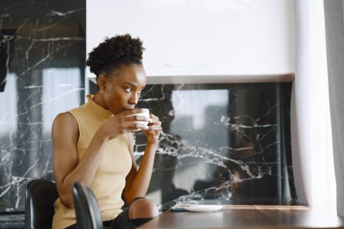 Free A young black woman sipping a hot drink while seated at a table in a stylish indoor setting. Stock Photo