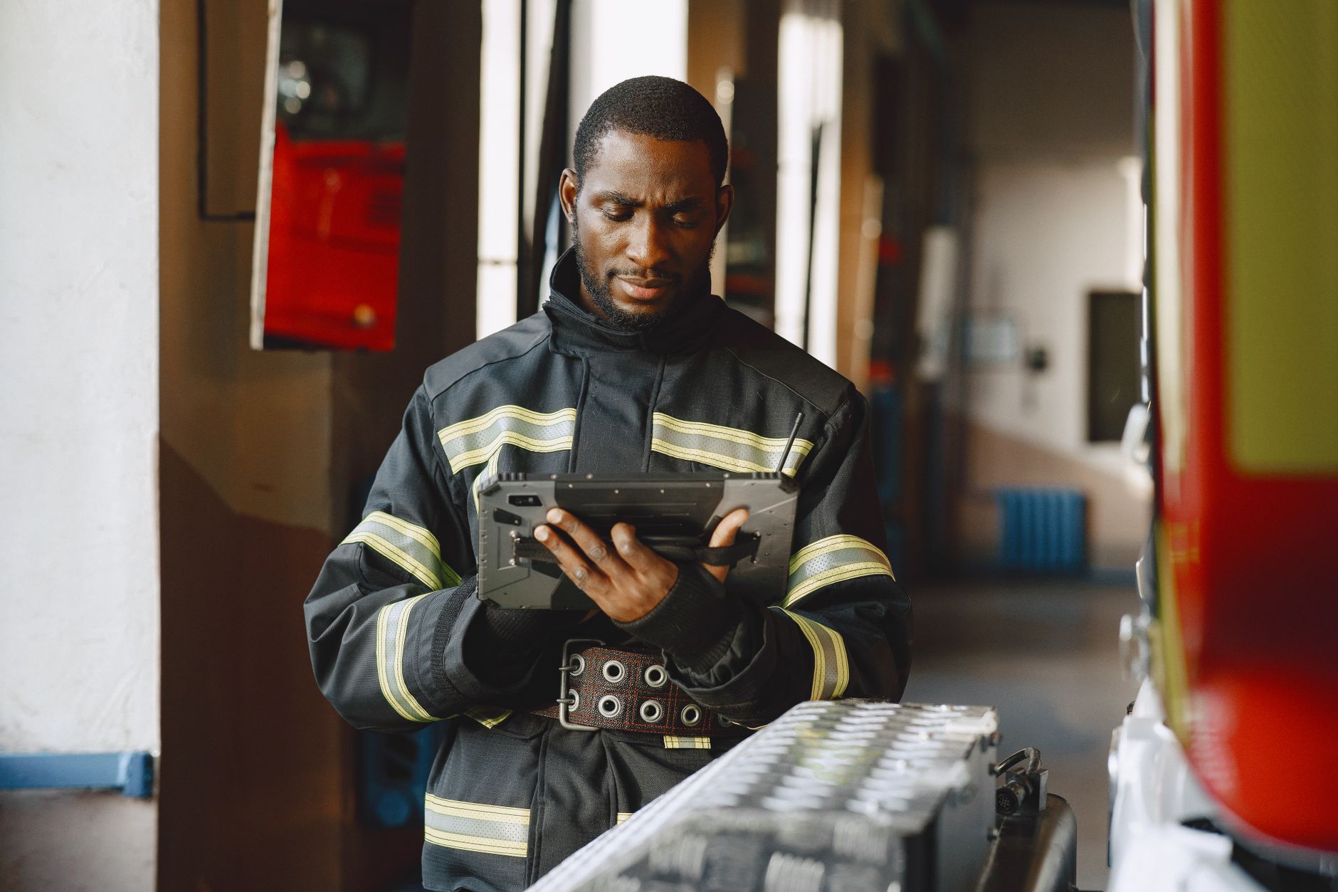 African American firefighter in uniform using a tablet inside a fire station.