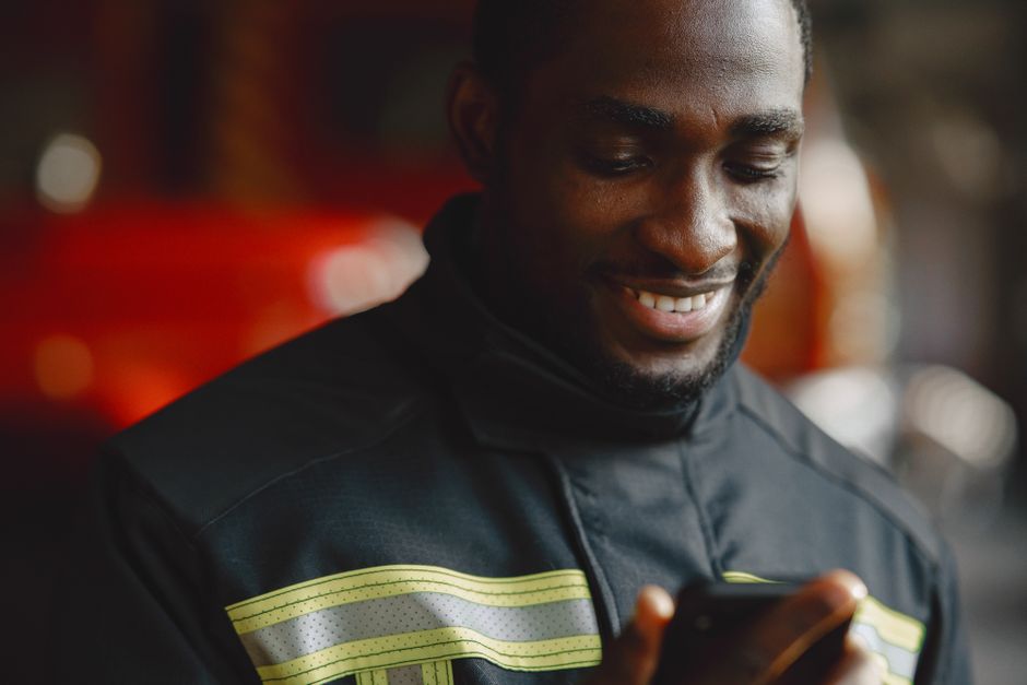Close-up of a firefighter smiling while using a smartphone indoors.