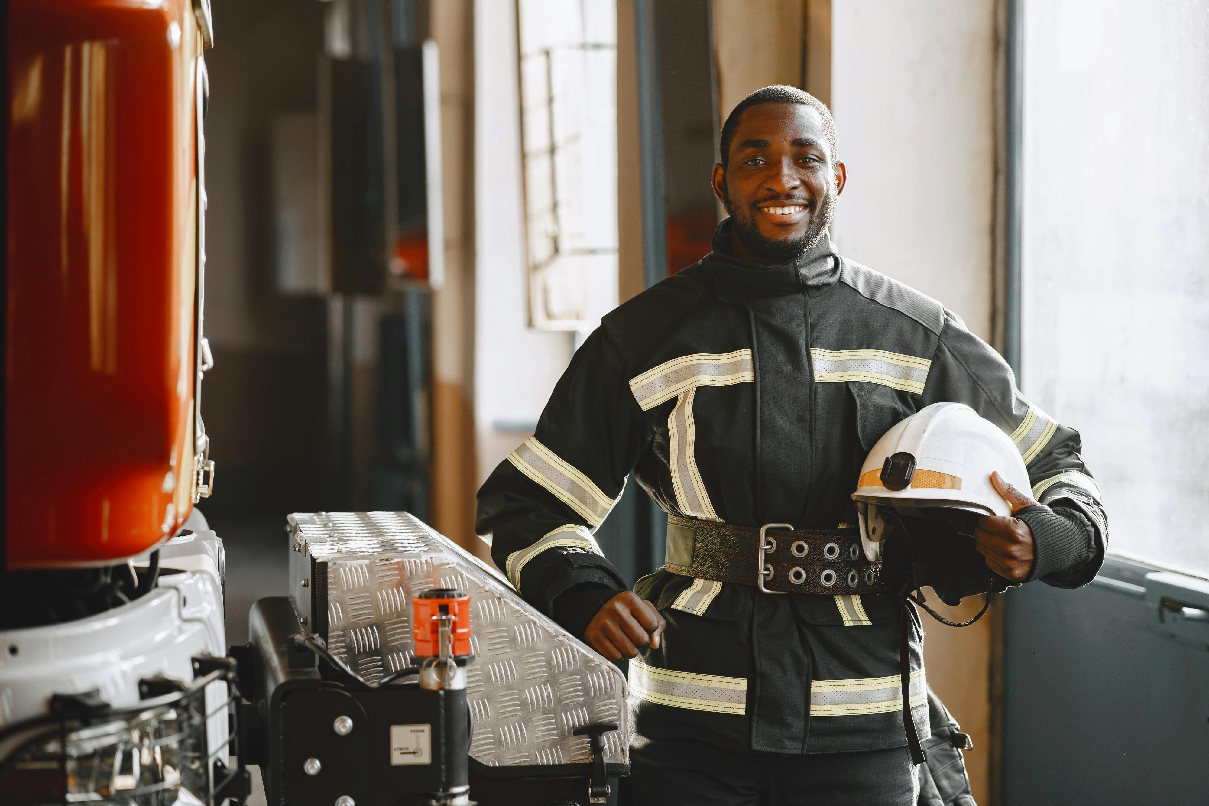 African American firefighter smiling, holding helmet indoors at fire station