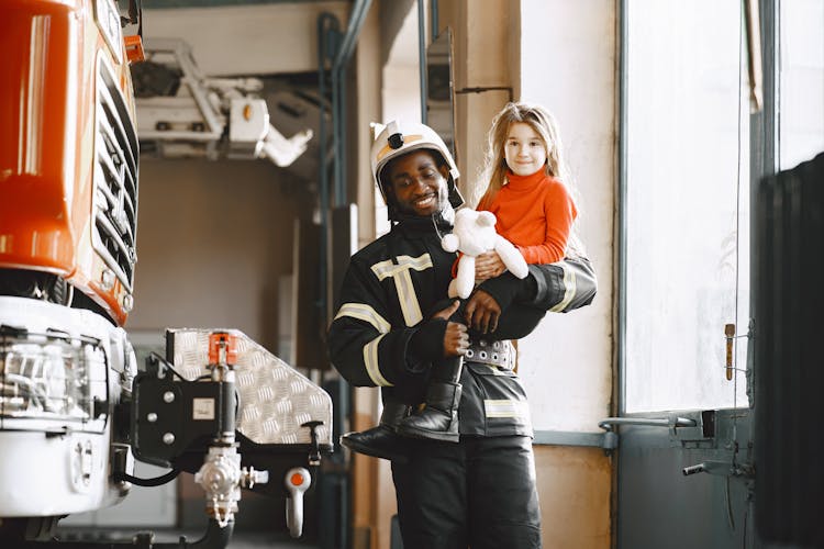 A Firefighter Holding A Little Girl And Showing Her Around The Garage At The Fire Station 