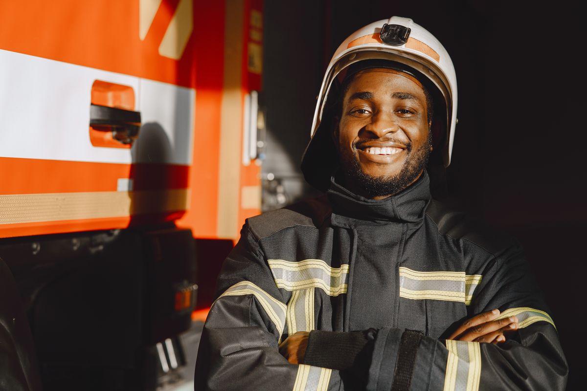 Smiling firefighter in gear facing the camera by a fire truck — firefighter mortgage programs from a lender who understands fire service