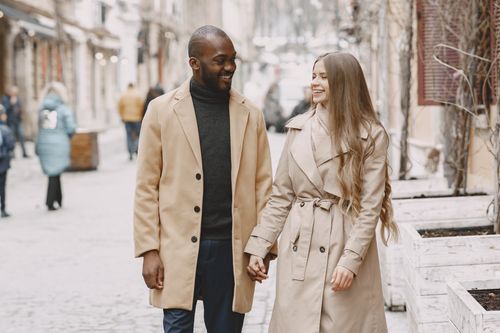 Free A joyful multiracial couple holding hands and walking in a winter urban setting. Stock Photo