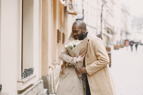 Free A happy couple embraces on a winter street, holding a bouquet of flowers. Stock Photo
