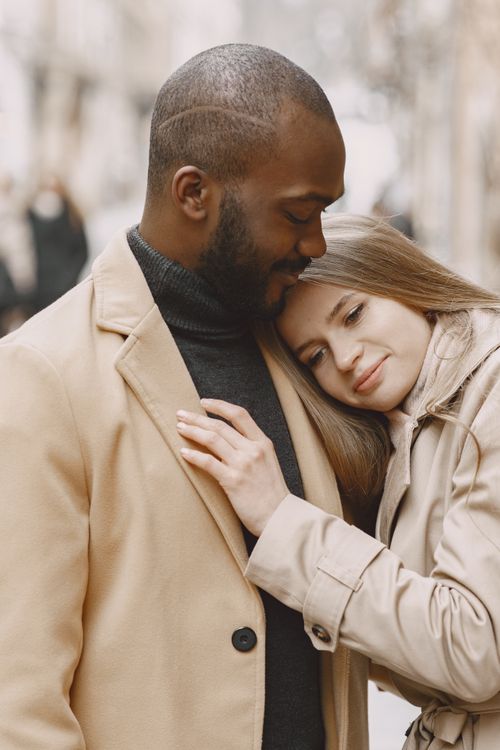 Free Heartwarming image of an interracial couple embracing outdoors, wearing winter coats. Stock Photo