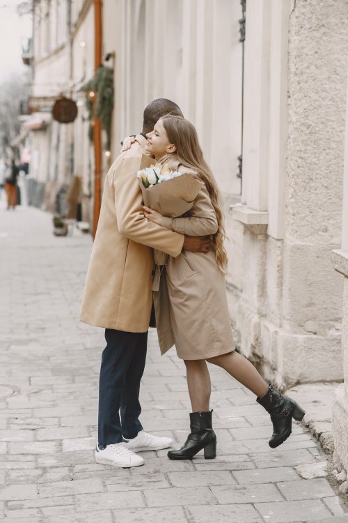 Free A couple embraces warmly on a cobblestone street, showcasing love and togetherness in winter. Stock Photo