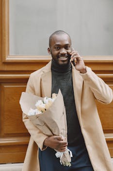 Smiling man holding a bouquet of flowers while talking on the phone outdoors.