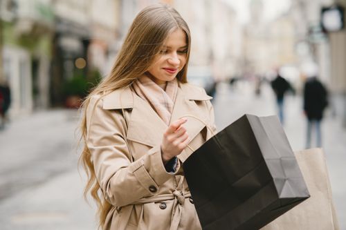 Free Caucasian woman smiling outdoors with shopping bags in winter attire. Stock Photo