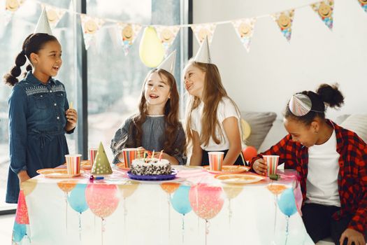 Joyful group of kids celebrating a birthday indoors with cake and party hats.