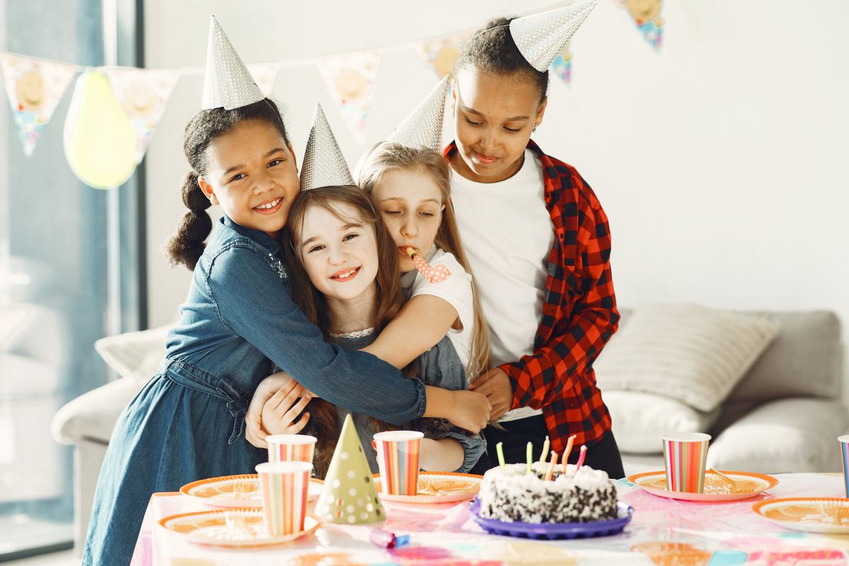 Group of kids enjoying a fun birthday party with cake and hats indoors. Stock Photo.