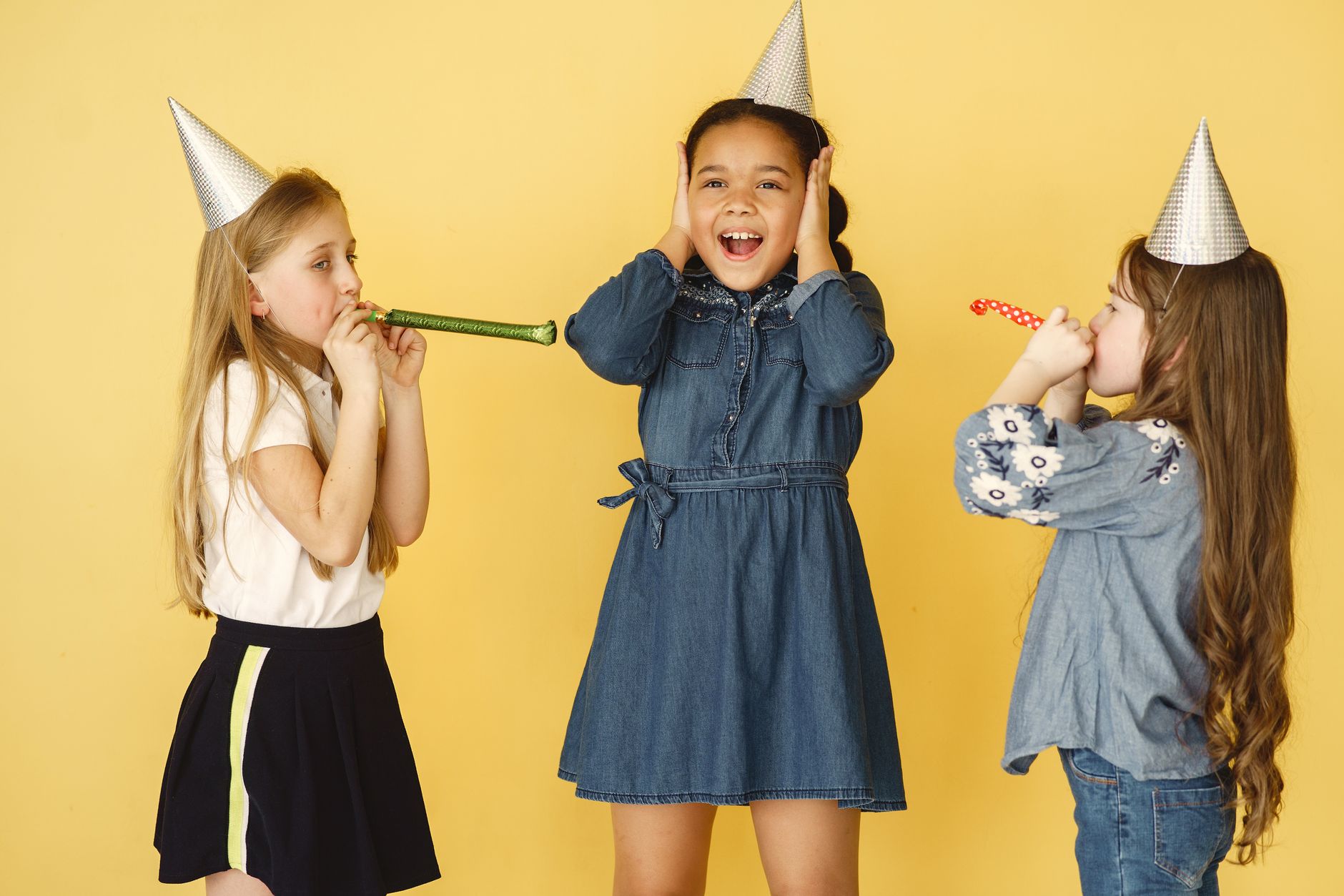 juggler for kids party cairo — Three children joyfully celebrate with party hats and streamers against a yellow background.