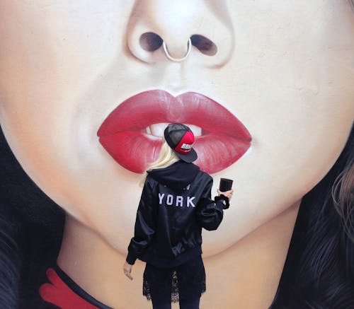 Woman in Black Jacket Standing near Modern Graffiti of Woman's Face