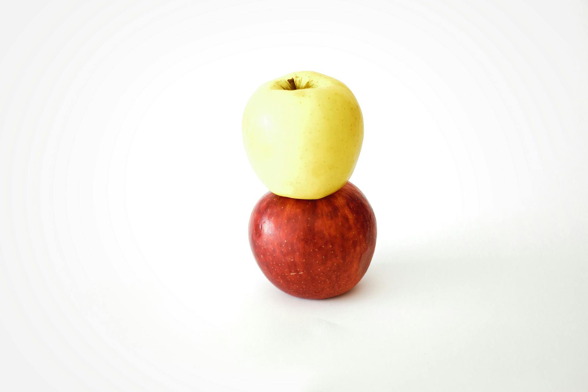 Two apples stacked on a white surface, showcasing balance and simplicity.