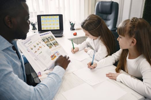 A teacher instructing two young students in a classroom environment.