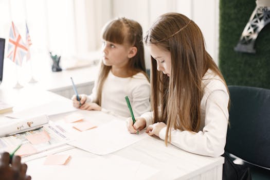 Two girls focus on writing in a classroom setting with educational materials around them.