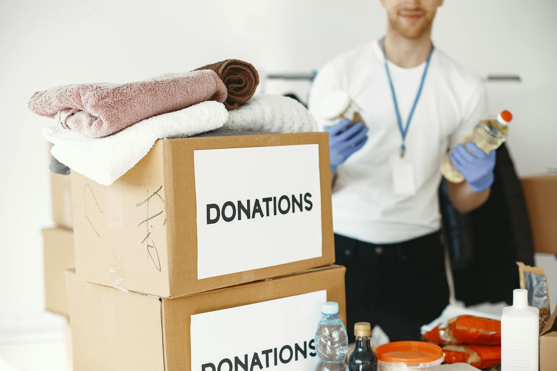 A volunteer organizing donation boxes filled with clothes and essential supplies indoors.