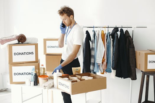 A volunteer organizes donation boxes and clothes while making a phone call in a bright room.