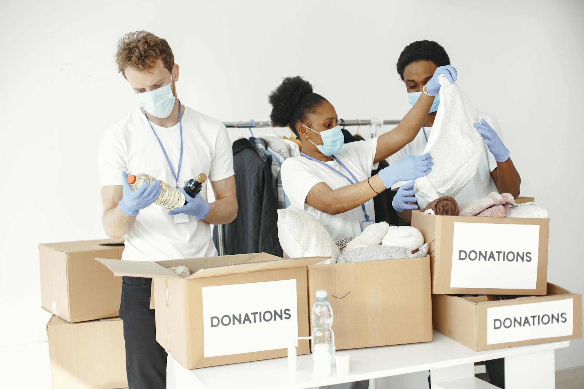 Volunteers wearing masks sort clothes and essentials into donation boxes, promoting charity and safety.