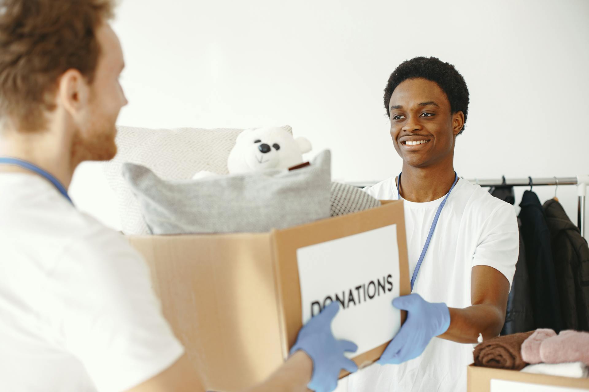 Two volunteers joyfully handing and receiving donation boxes full of clothes and toys.