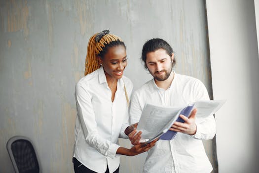 Two professionals reviewing documents in a modern office setting. Multicultural workplace.
