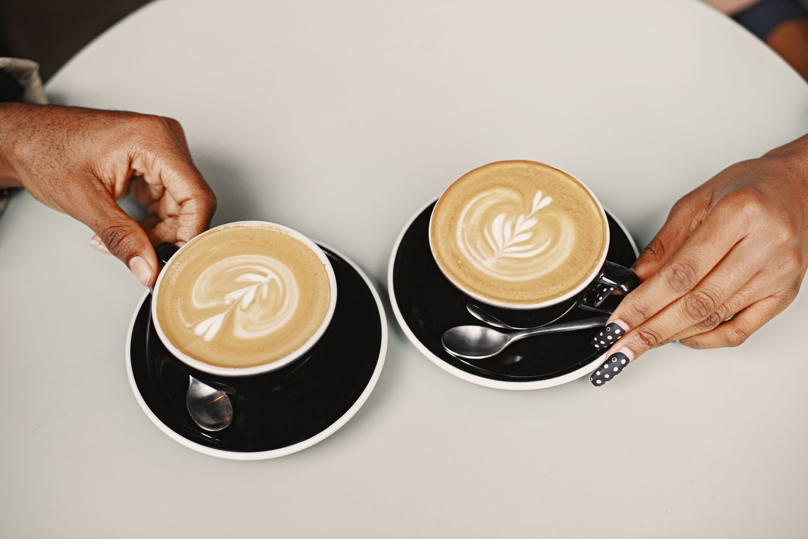 Two lattes with foam art held in black cups and saucers